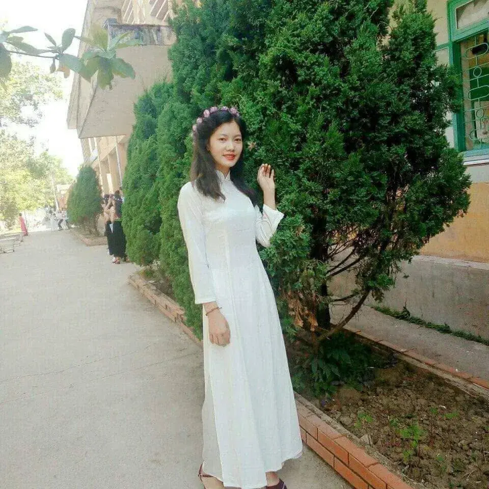 Lì Gò Pa standing outdoors in a white áo dài
